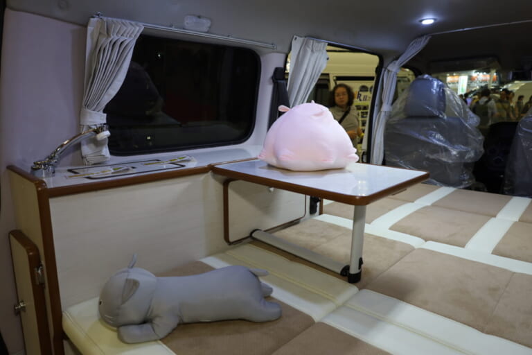 テーブルは、シンクを装備するキャビネットに接続する形で設置。キャビネットの天板もテーブルの一部になり広々と使える。料理にこだわる女性バンライファーも車内調理が楽しめそうだ。|「えぇーっ もはや家だぞ…」普通のトヨタ車と思いきや…暮らせるレベルの車内に驚いた。キッチン・冷蔵庫・クーラー・電源にベッドまで!