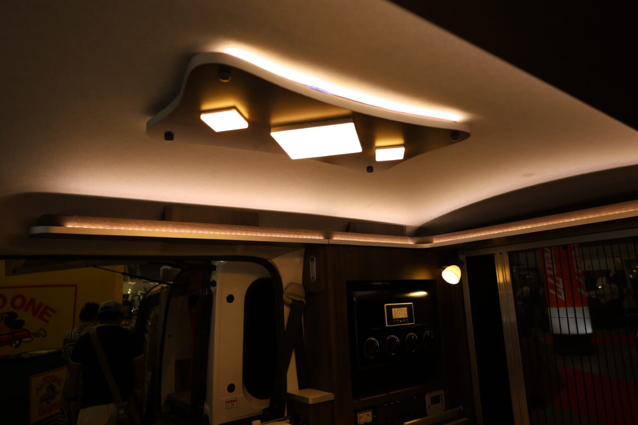 オプションで天井照明、左右スポットライト、間接照明を用意。照明器具もおしゃれで豪華。夜が楽しみになる雰囲気づくりができそうだ。｜「これは凄いぞ…」ヤバい軽キャンパーがデビュー。ニューモデルは、めっちゃ嬉しい機能付き。高級感のある落ち着いた、開放的な室内空間は圧巻。