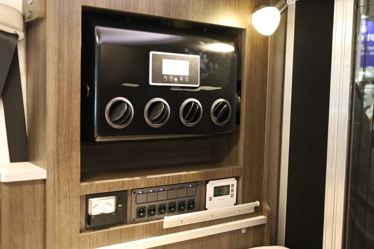 東京キャンピングカーショー2025の参考展示車は、リア右側のインテリアに車載用クーラーをビルトイン。その下にはバッテリー残量計や集中スイッチパネルを配置し、電化の充実ぶりをうかがわせる。｜「これは凄いぞ…」ヤバい軽キャンパーがデビュー。ニューモデルは、めっちゃ嬉しい機能付き。高級感のある落ち着いた、開放的な室内空間は圧巻。