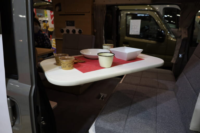 テーブルは室内のレイアウトに合わせて前後左右に自由に動かせるマルチウェイテーブルを標準装備。未使用時はベッドマット下スペースに収納できる。|「軽とは思えない」チープさ排除でブッ刺さる、まるで走るタイニーハウス。普通に手の届く価格帯が嬉しい軽キャンパー。