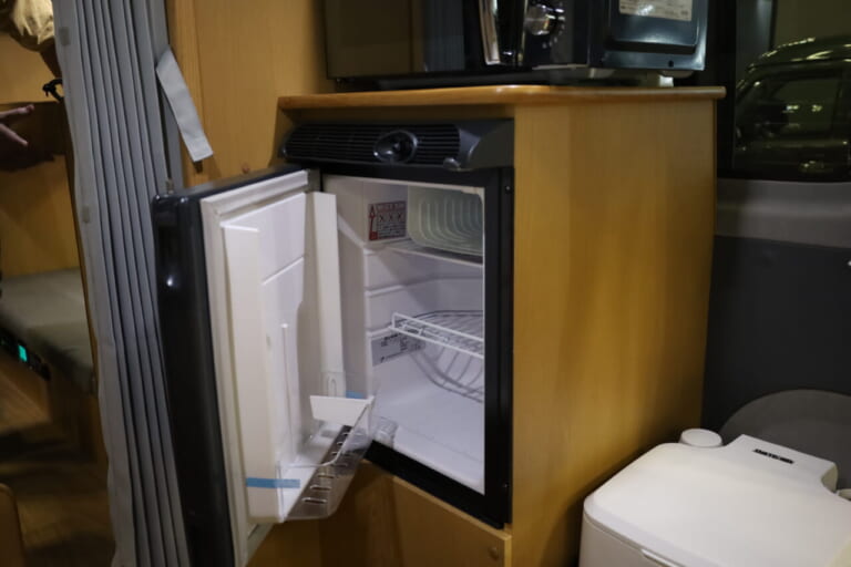 車内調理で活躍する電子レンジを装備。電子レンジの下には40Lの横開き冷蔵庫を標準装備。庫内から出したものをすぐに調理できる。ともに標準装備品だ。｜「おいおい、これは住めちゃうぞ」クルマの中に電子レンジや冷蔵庫、キッチンまで装備。もはや1Kの部屋みたいで便利に使えそう。