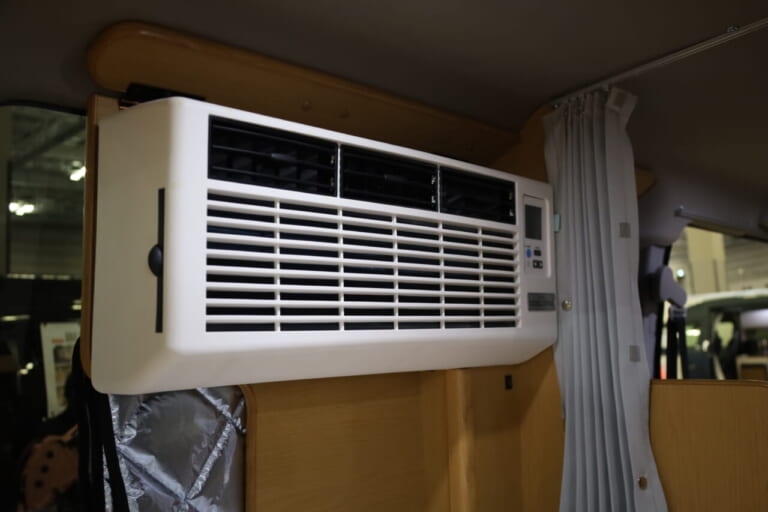 リア左側には12Vクーラーを装備。室外機は床下収納庫に収め、すっきりと設置している。｜「おいおい、これは住めちゃうぞ」クルマの中に電子レンジや冷蔵庫、キッチンまで装備。もはや1Kの部屋みたいで便利に使えそう。