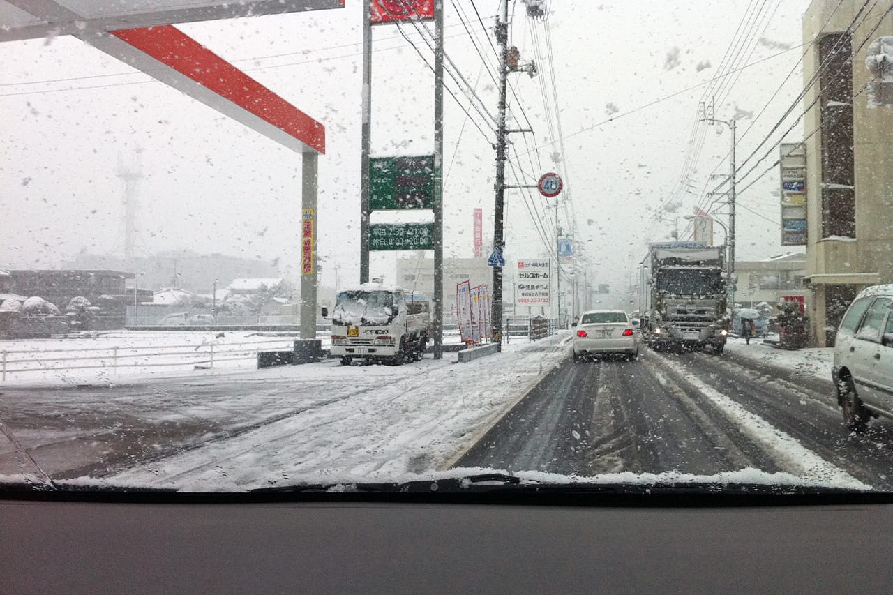 雪が降る中を走行する車｜「ノーマルタイヤで走行はNG」では人気の布製タイヤチェーンはチェーン規制区間で通行OK？ 簡単装着・手軽で便利なんだけど…。