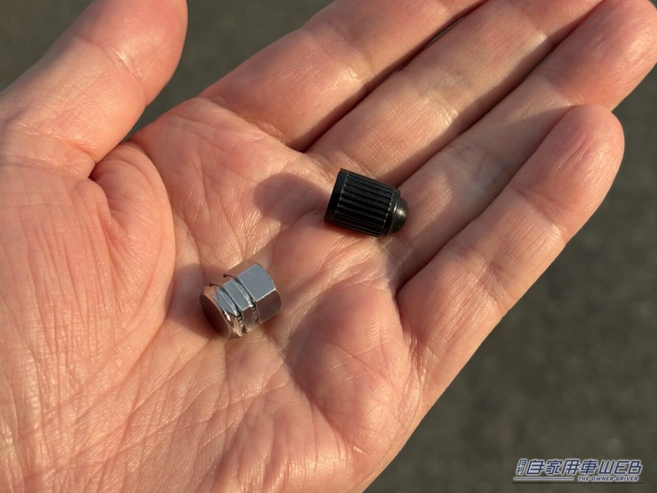 タイヤから外した純正の黒いバルブキャップと、エーモンのエアバルブキャップ(8828)を手のひらに乗せている画像|「そこに付けるんだ?」「意外と雰囲気変わるね」愛車にさりげないアクセント。分かる人には分かるお手軽カスタムパーツを紹介。
