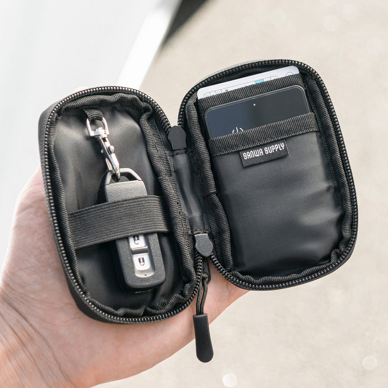 サンワサプライ スマートキーケース（200-CAR105）のファスナーを開いて、手に持っている｜「コレ,工夫がスゴい…」防水素材&止水ファスナーで中身も安心。クルマに乗る人にオススメ。ちょうどいい収納力のスマートキーケースを紹介