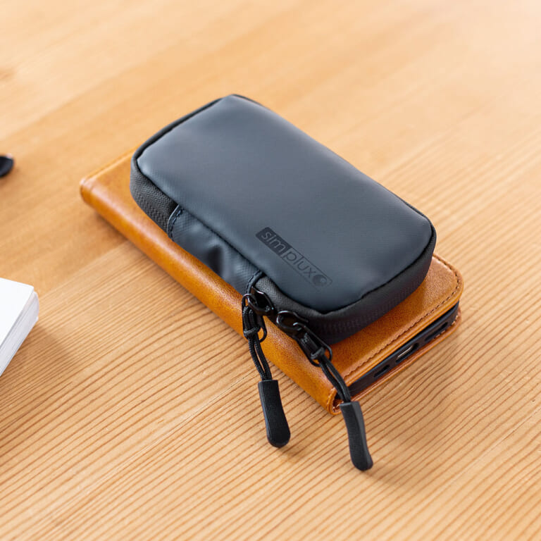 サンワサプライ スマートキーケース（200-CAR105）をスマートフォンと重ねて置いた画像｜「コレ,工夫がスゴい…」防水素材&止水ファスナーで中身も安心。クルマに乗る人にオススメ。ちょうどいい収納力のスマートキーケースを紹介