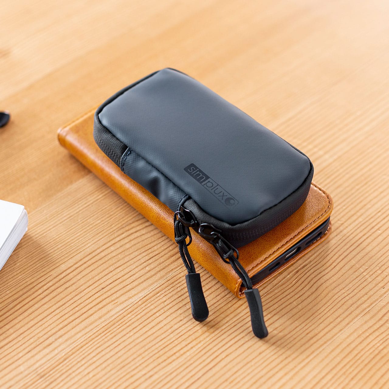 サンワサプライ スマートキーケース（200-CAR105）をスマートフォンと重ねて置いた画像｜「コレ,工夫がスゴい…」防水素材&止水ファスナーで中身も安心。クルマに乗る人にオススメ。ちょうどいい収納力のスマートキーケースを紹介