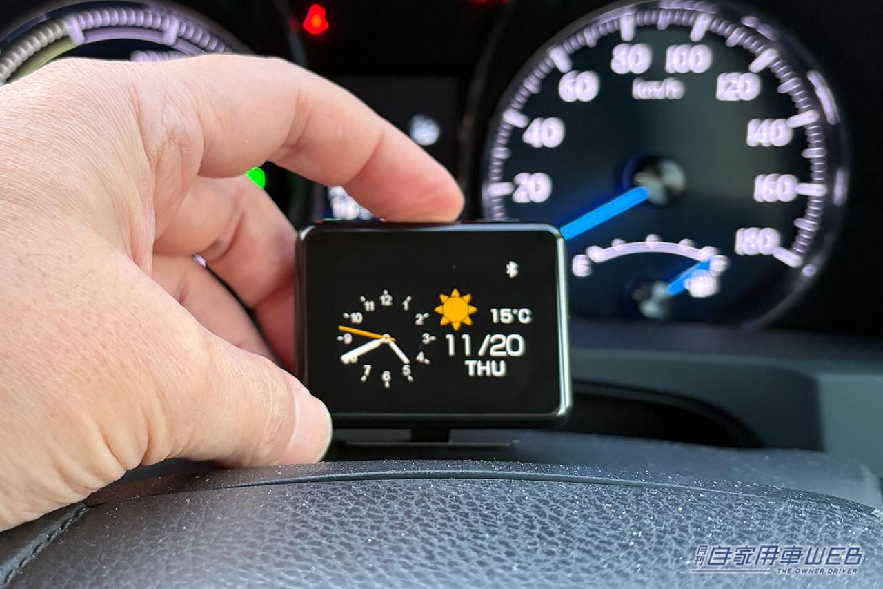 クルマのインパネ付近に設置されたカシムラのスマートクロック(AK-230)の本体上部にあるボタンを操作する画像|「結果、大正解でした」小型モニターを車内に設置。ドライブ中に情報を表示。あらゆる車種に対応するガジェットを購入! 実際に使用した印象をレポート